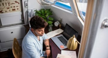 Man taking notes in a notebook while next to his laptop